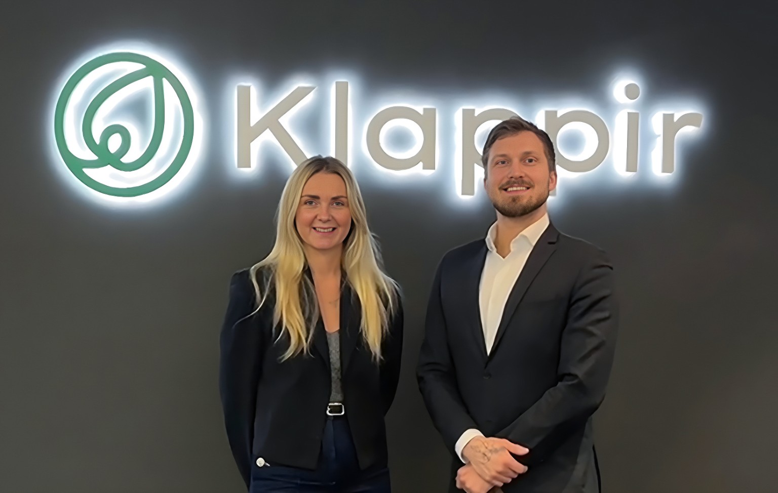 Two people standing in front of the Klappir logo